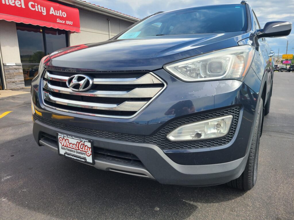 Close-up of a dark blue Hyundai SUV at a car dealership with a red Wheel City Auto sign in the background.