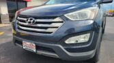 Close-up of a dark blue Hyundai SUV at a car dealership with a red Wheel City Auto sign in the background.