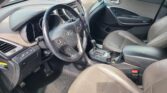 Interior view of a car's driver side: steering wheel with control buttons, dashboard, and center console including gear shifter and cup holders.