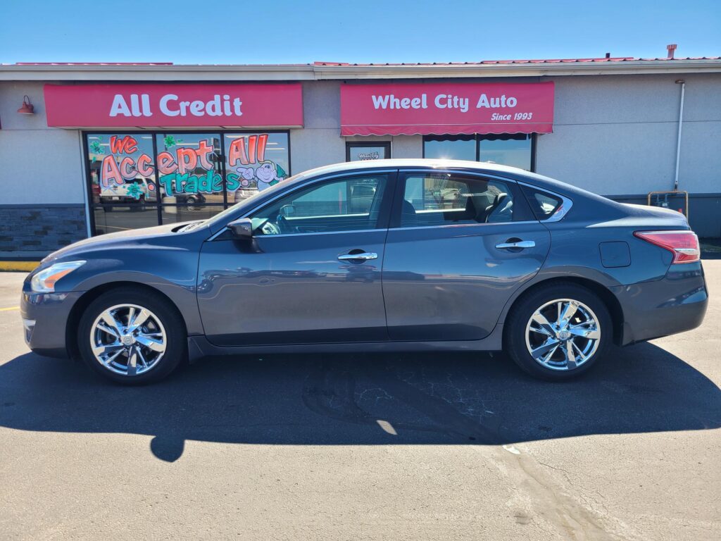 Gray sedan parked in front of a storefront with pink awnings reading 'All Credit' and 'Wheel City Auto.'