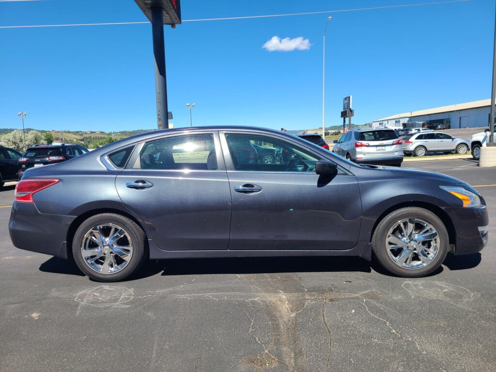 Gray sedan in a parking lot with other cars and a clear blue sky behind it.