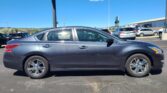 Gray sedan in a parking lot with other cars and a clear blue sky behind it.