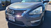 Front three-quarter view of a dark gray Nissan SUV parked at a dealership, showing a Wheel City Auto Finance license plate frame on the front bumper and a vehicle info sticker on the windshield.