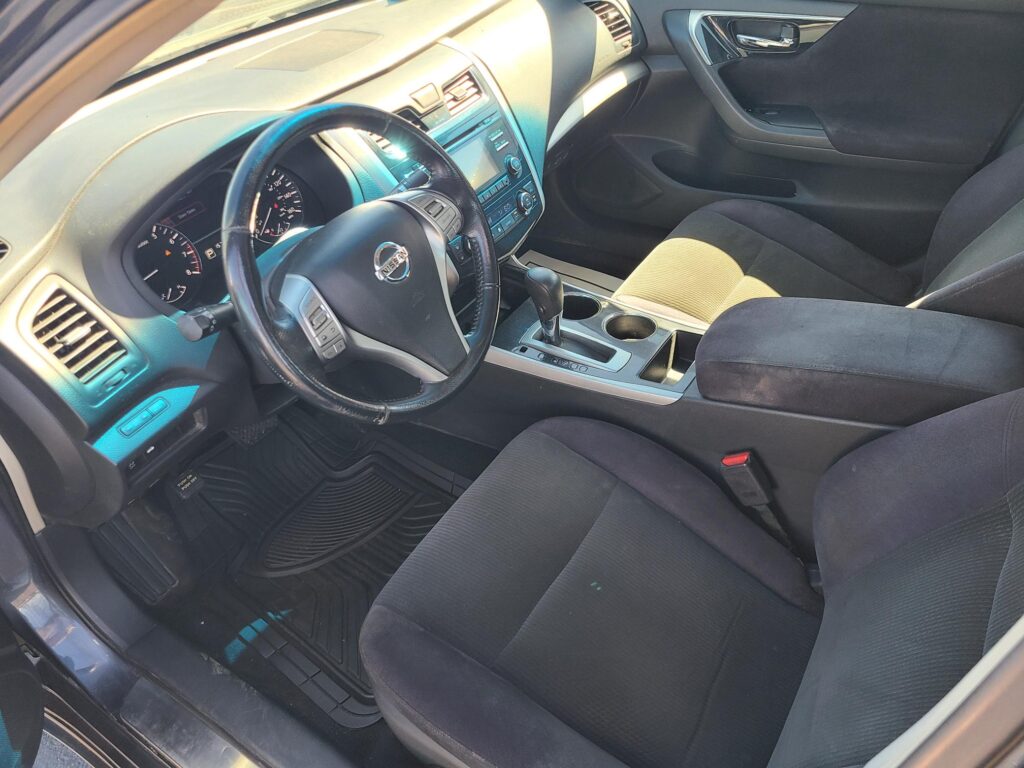 Interior of a Nissan car: steering wheel with logo, center console, and front seats visible from the driver's side door (gear shift and controls shown).