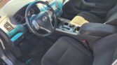 Interior of a Nissan car: steering wheel with logo, center console, and front seats visible from the driver's side door (gear shift and controls shown).