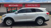 Silver SUV parked in front of a car dealership storefront with red 'All Credit' and 'Wheel City Auto' signs above the windows