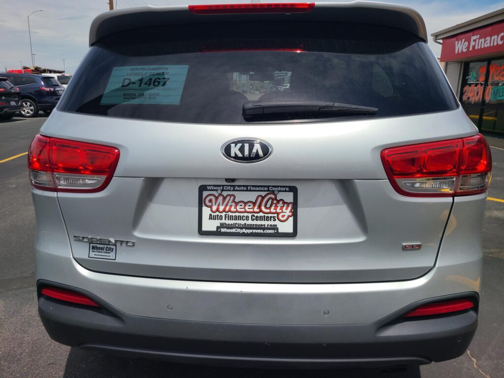 Rear view of a silver Kia SUV at a dealership, with Wheel City Auto Finance Centers signage on the license plate frame and a green sale sticker in the rear window.