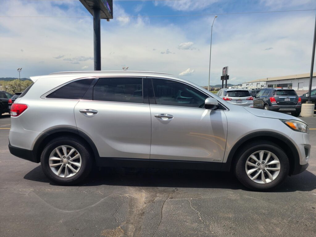 Side view of a silver SUV in a parking lot, with other cars and a building in the background.