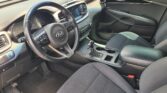 Front interior of a Kia SUV showing steering wheel, center touchscreen, gear shifter, and black cloth seats in a clean cabin.