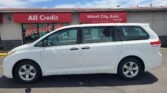 White minivan parked in front of a storefront with red All Credit and Wheel City Auto signs above the entrance.