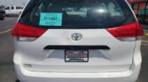 Rear view of a white Toyota Sienna with a teal dealer placard visible in the rear window showing South Dakota Vehicle Dealer D-1467 and Wheel City Auto Finance Centers groundplate area.
