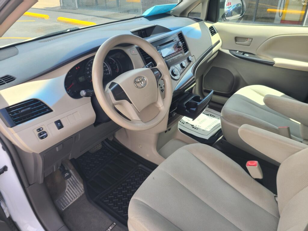 Interior of a beige Toyota car showing steering wheel, dashboard, and front seats from the driver's side