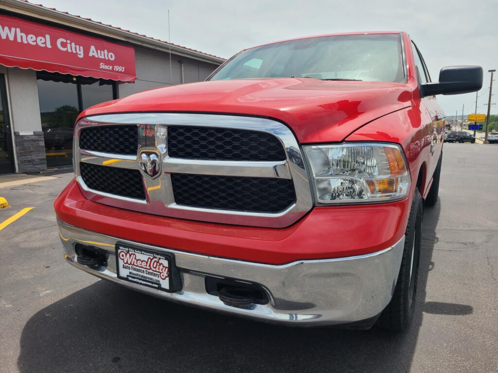 Close-up of a red pickup truck front end in a dealership lot, with a Wheel City Auto sign in the background.