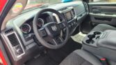 Interior of a red pickup truck showing the driver’s area: steering wheel, dashboard with infotainment screen, and center controls visible from the passenger seat angle.