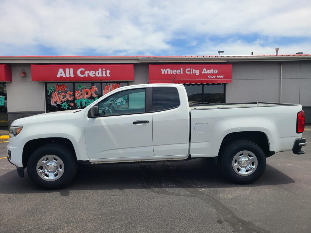 White pickup truck parked in front of a red storefront with signs reading All Credit and Wheel City Auto.Since 1993 is also visible on the sign?