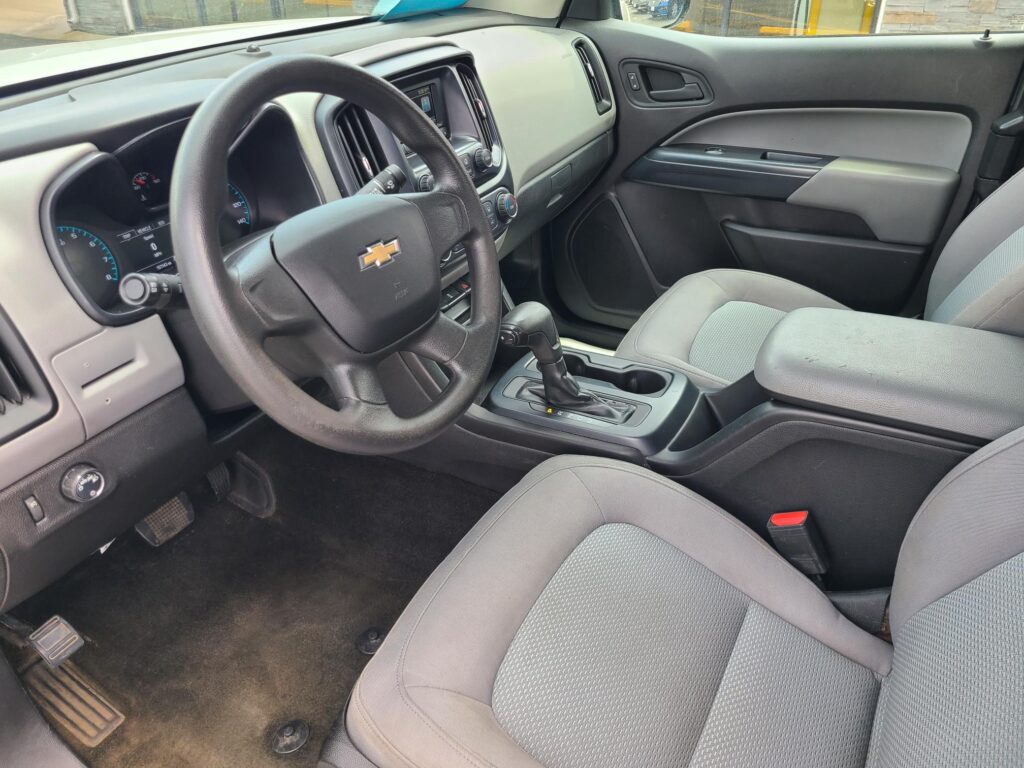 Interior of a car focusing on the driver's side: steering wheel, instrument cluster, center console, and gray fabric seats.