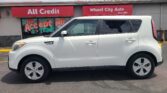 White SUV parked in front of a storefront with red signs that read 'All Credit' and 'Wheel City Auto' (Since 1993).