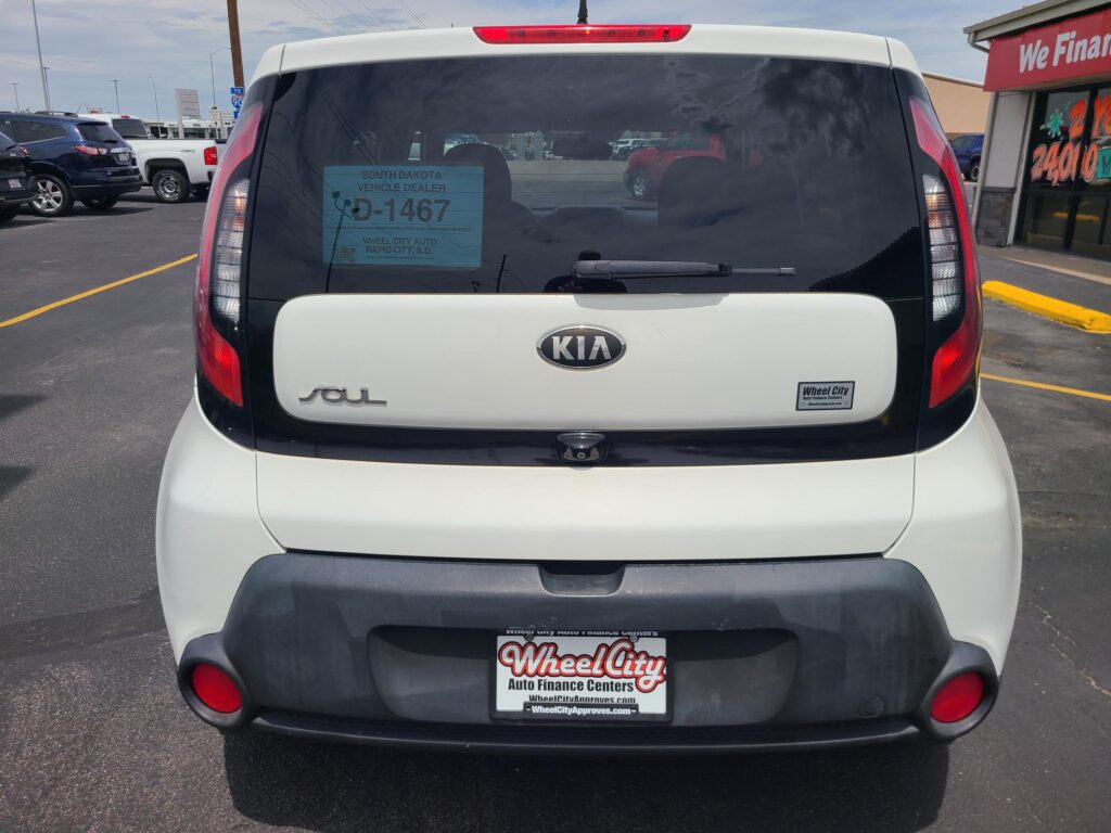Rear view of a white Kia Soul in a dealership lot, with a blue dealer sticker on the rear window reading 'South Dakota Vehicle Dealer D-1467'.