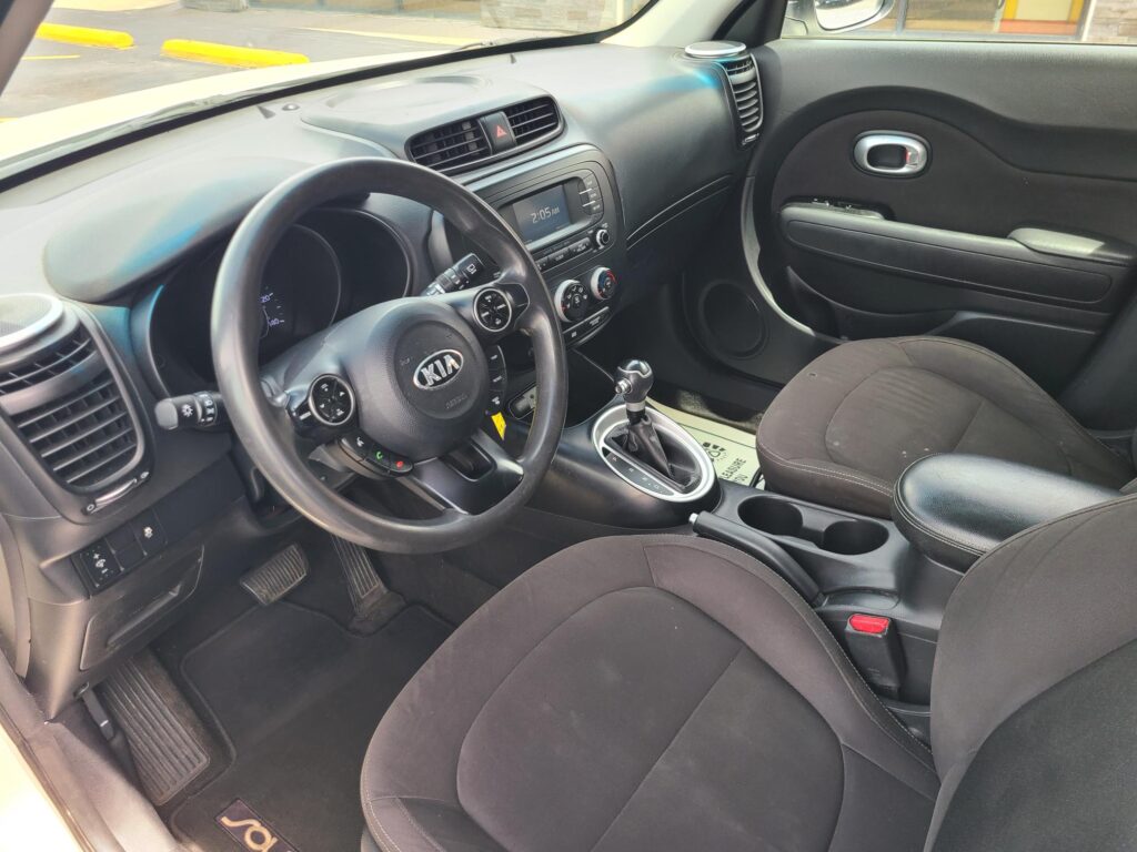 Interior of a Kia car focusing on the dashboard, steering wheel, and center console with an automatic shifter, in a parked position.