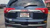 Rear view of a blue GMC Acadia SUV, showing the tailgate, rear windshield wiper, and red taillights in a car lot. License plate frame reads Wheel City Auto Finance Centers.