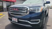 Front view of a dark gray GMC pickup truck parked in front of a red Wheel City Auto storefront awning with chrome grille and large GMC emblem.