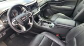 Interior of a GMC vehicle: driver’s seat, steering wheel, center touchscreen display, climate controls, and black leather upholstery with stitching.