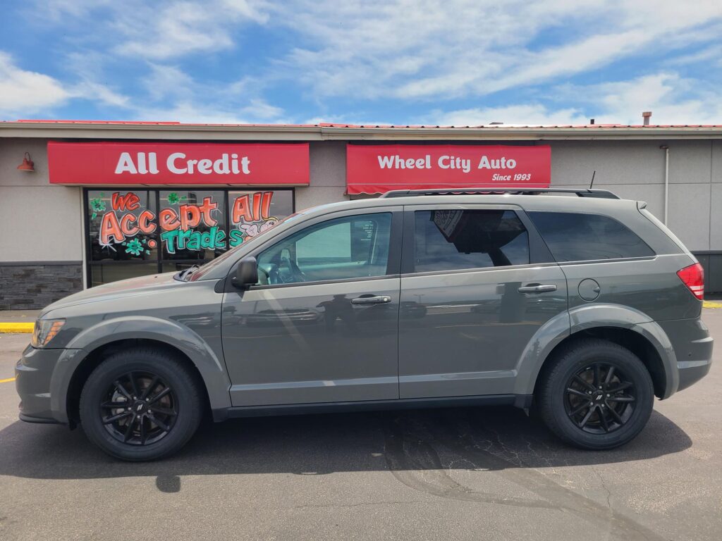 Front of a car dealership with red All Credit and Wheel City Auto signs; a gray SUV is parked in front.
