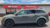Front of a car dealership with red All Credit and Wheel City Auto signs; a gray SUV is parked in front.