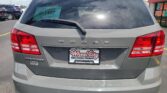 Rear view of a gray Dodge Journey SUV in a dealership lot, teal D-1467 decal visible on the rear window, Wheel City license plate frame.