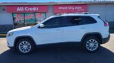 White SUV parked in front of a storefront with pink signs reading 'All Credit' and 'Wheel City Auto Since 1993'; front window mural says 'We Accept All Trades'.