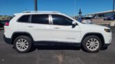 Side view of a white Jeep Cherokee SUV with roof rails parked in a lot, visible windows and wheels