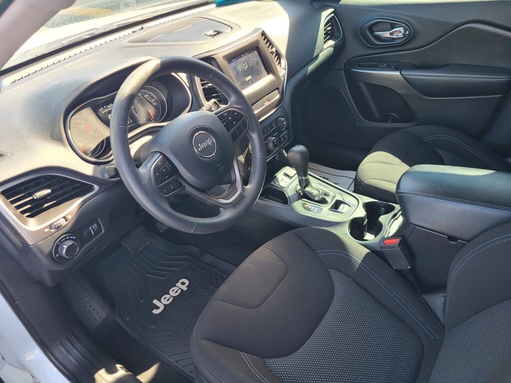 Jeep interior with steering wheel, central touchscreen, and gear shift seen from the passenger side start area.