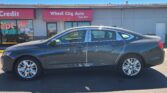 Dark gray Chevrolet Impala sedan parked in front of Wheel City Auto storefront with a pink awning that reads since 1993.