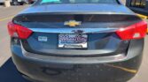 Rear view of a blue Chevrolet sedan in a dealership lot, with Wheel City Auto Finance Centers plate frame and teal window sticker visible on the rear window.