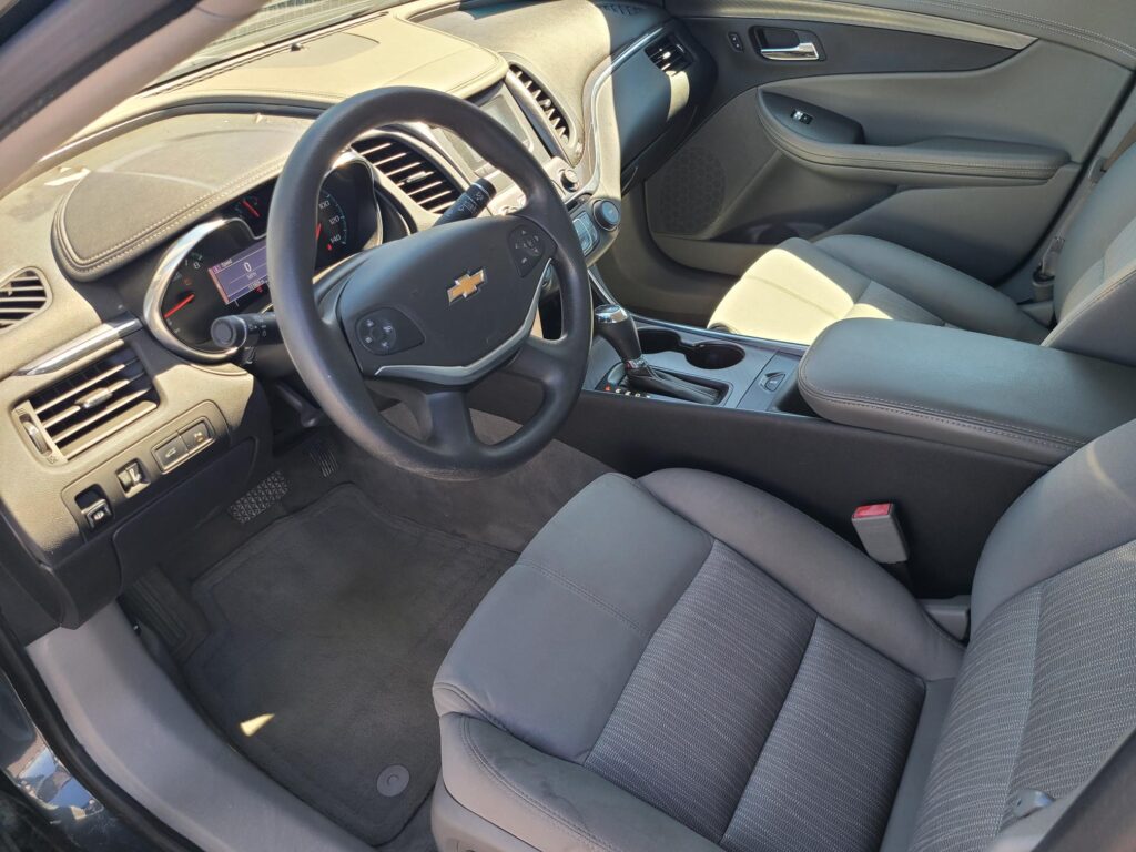 Interior of a Chevrolet sedan: steering wheel with logo, digital gauge cluster, center console, and gray fabric seats.