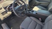 Interior of a Chevrolet sedan: steering wheel with logo, digital gauge cluster, center console, and gray fabric seats.