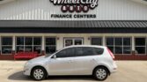 Silver hatchback parked in front of Wheel City Auto Finance Centers storefront with a red bench nearby.