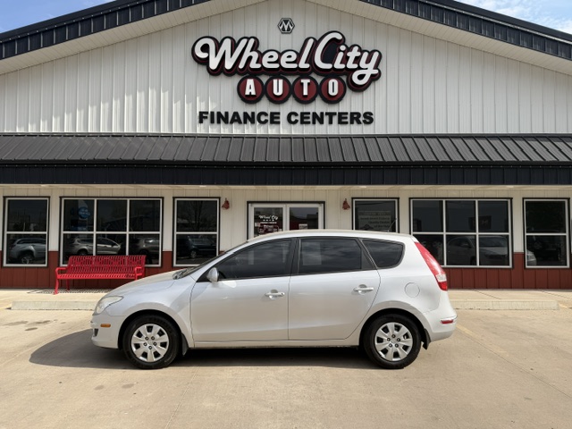 Silver hatchback parked in front of Wheel City Auto Finance Centers storefront with a red bench nearby.