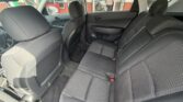 Rear seating area of a dark cloth‑upholstered sedan, showing three seats, headrests, and accessible seat belts; front seats and door panels visible, through windows to a street scene.