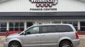 Silver minivan parked in front of Wheel City Auto Finance Centers dealership, with the storefront and large sign visible.
