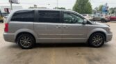 Side view of a silver minivan parked in a parking lot, with other cars and trees in the background.