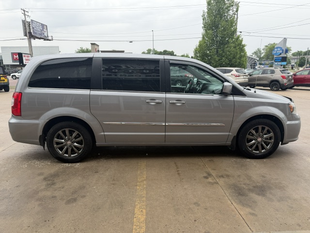 Side view of a silver minivan parked in a parking lot, with other cars and trees in the background.