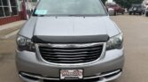 Front view of a silver Chrysler minivan in a parking lot, showing a large chrome grille, bumper guard, and a WheelCity Auto Finance Centers license plate.