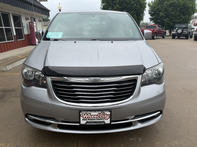 Front view of a silver Chrysler minivan in a parking lot, showing a large chrome grille, bumper guard, and a WheelCity Auto Finance Centers license plate.