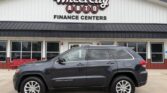 Dark gray Jeep Grand Cherokee SUV parked in front of Wheel City Auto Finance Centers storefront sign(s).