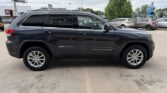 Side view of a black Jeep Grand Cherokee SUV parked in a lot, with tinted windows and alloy wheels visible.