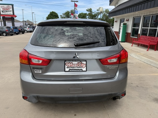 Rear view of a silver Mitsubishi Outlander Sport SUV in a dealership lot, with a Wheel City Auto Finance Centers license plate frame.