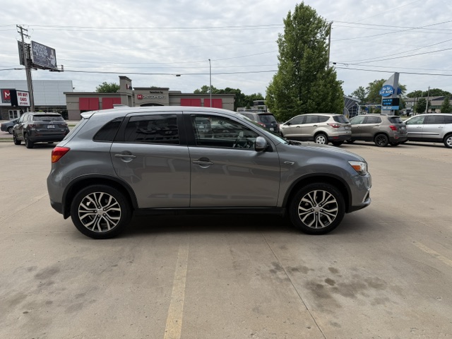 Side view of a gray midsize crossover SUV parked in a parking lot with storefronts in the background while other cars surround it.