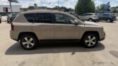 Side view of a beige Jeep Compass SUV parked in a sunny lot, with other cars and a clear blue sky in the background.