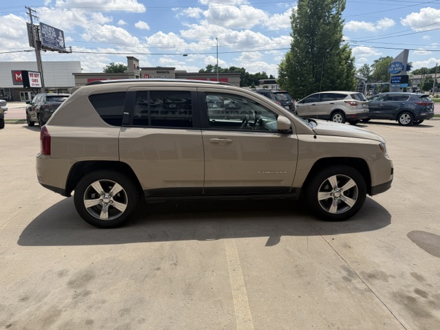 Side view of a beige Jeep Compass SUV parked in a sunny lot, with other cars and a clear blue sky in the background.